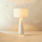 Clérachic mid-size white drum shade glowing warm over a tapering cream base on three pointed metal feet.