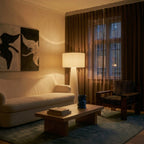 Clérachic floor lamp glowing at dusk in a living room, white drum shade beside a bouclé sofa and brown sheer curtains.