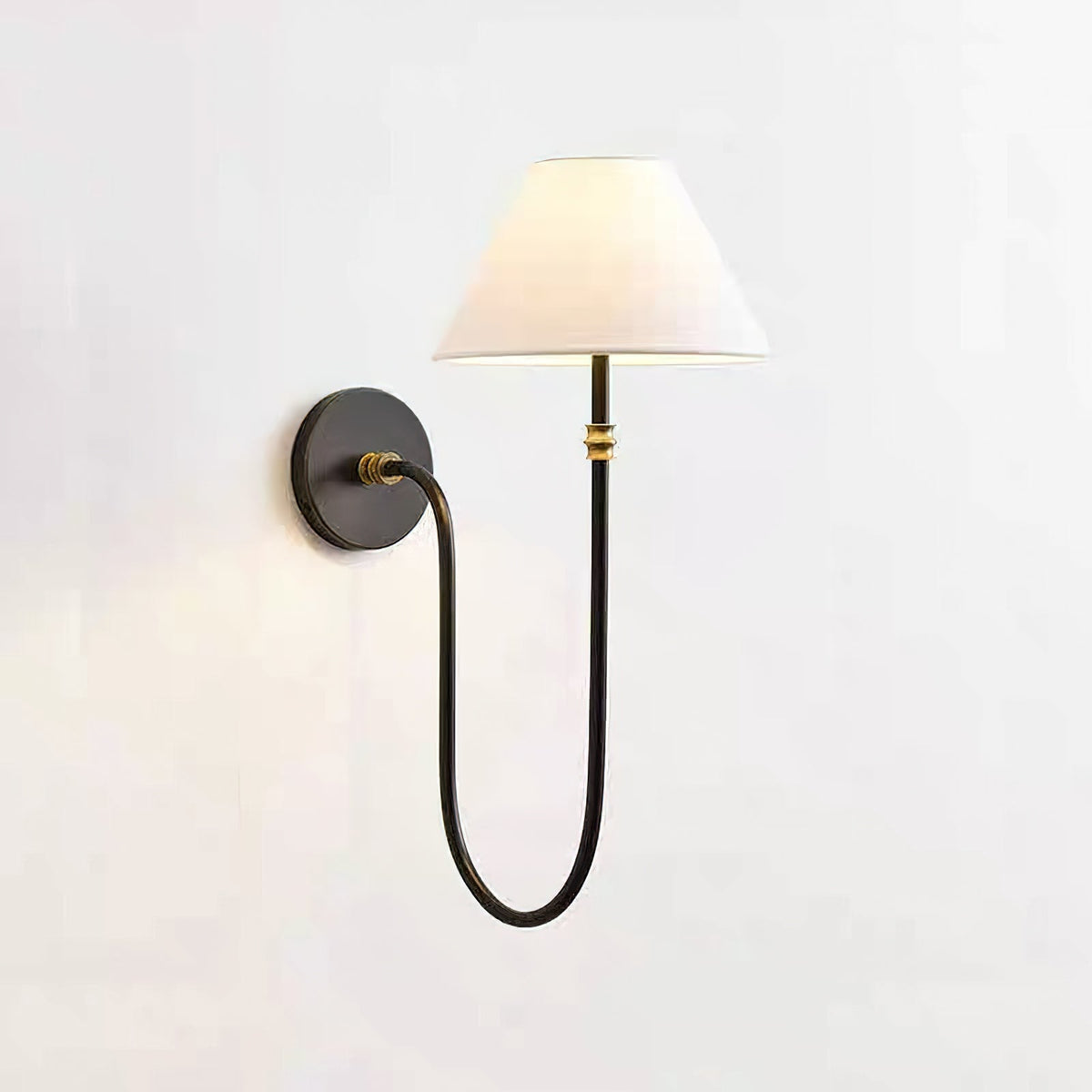 This Clérachic wall light in black and white, lit softly, with a curved black arm looping down from a round plate to a tapered shade.