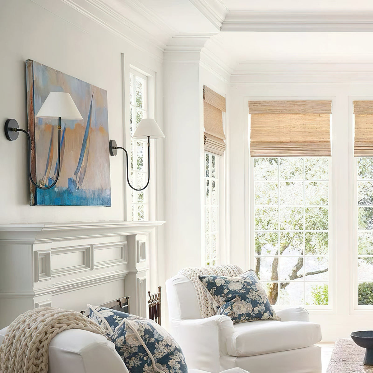 Two black Clérachic wall lights with white shades flanking a sailing painting in a bright room, above a white panelled mantel and armchair.