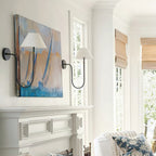 Black and white Clérachic wall lights on either side of a sailing painting, with a panelled mantel and a floral cushion below.