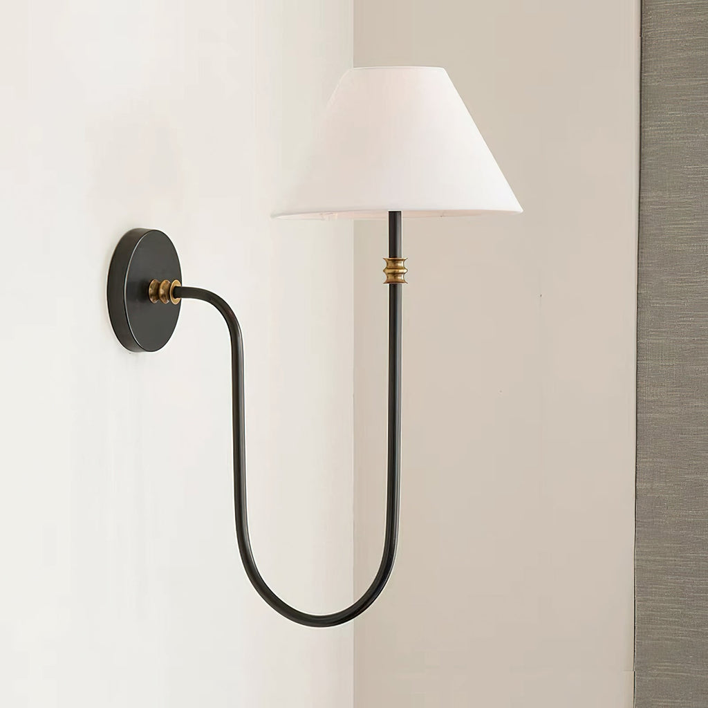 Side view of a black Clérachic wall light on a pale wall, with the U-shaped arm, small brass collar and white shade near a grey curtain.