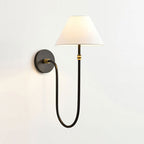 Black Clérachic wall light with a softly glowing white shade and small brass bands on the stem, against a plain light wall.