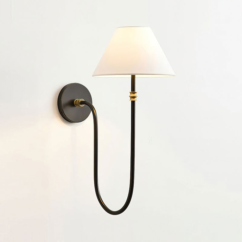 Black Clérachic wall light with a softly glowing white shade and small brass bands on the stem, against a plain light wall.
