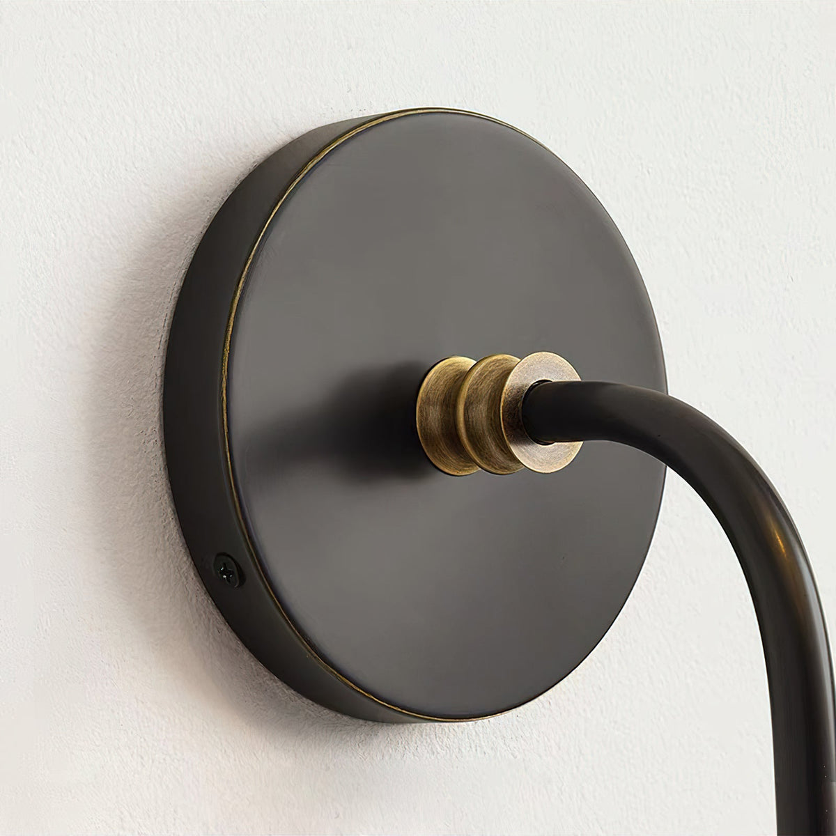 Close view of the round black backplate and curved arm of this Clérachic wall light, with a small brass collar at the join.
