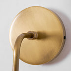 Close view of the brushed brass round backplate and the curved arm of this Clérachic wall light.