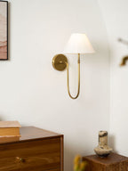 Smaller view of a brass Clérachic wall light with a white shade above a walnut chest of drawers and a stone vase.