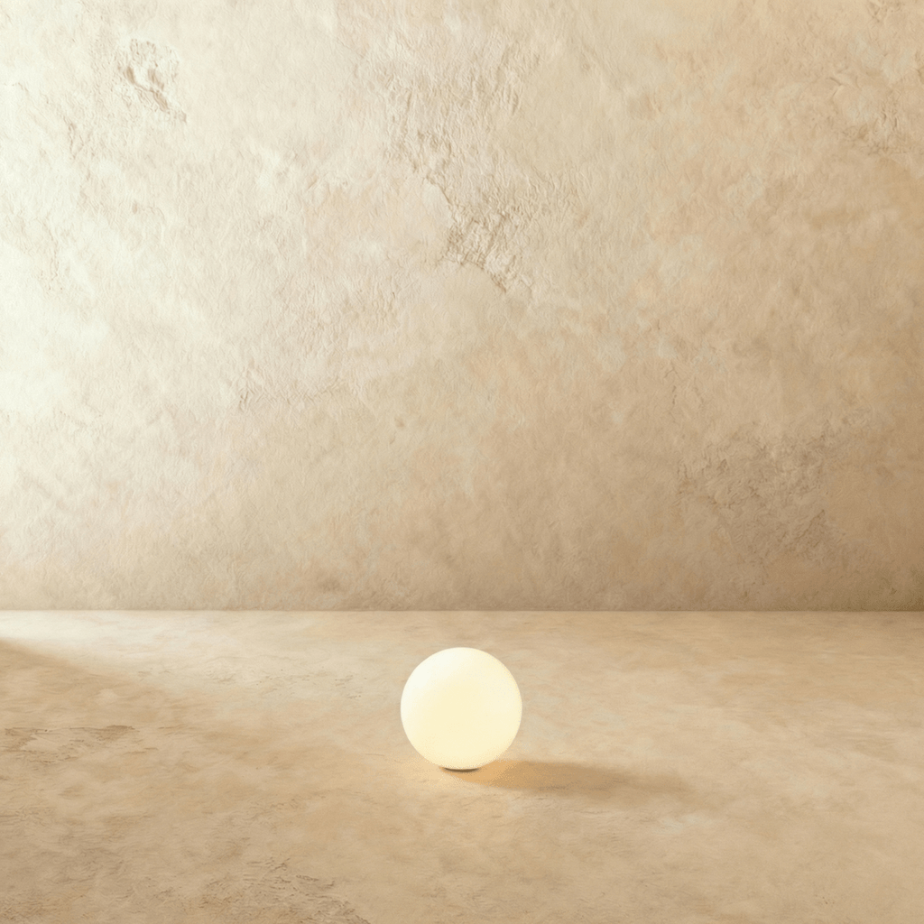 A small Clérachic glowing sphere floor lamp sits lit on a warm plaster floor against a matching wall.