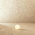A small Clérachic glowing sphere floor lamp sits lit on a warm plaster floor against a matching wall.
