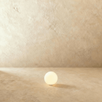 A small Clérachic glowing sphere floor lamp sits lit on a warm plaster floor against a matching wall.