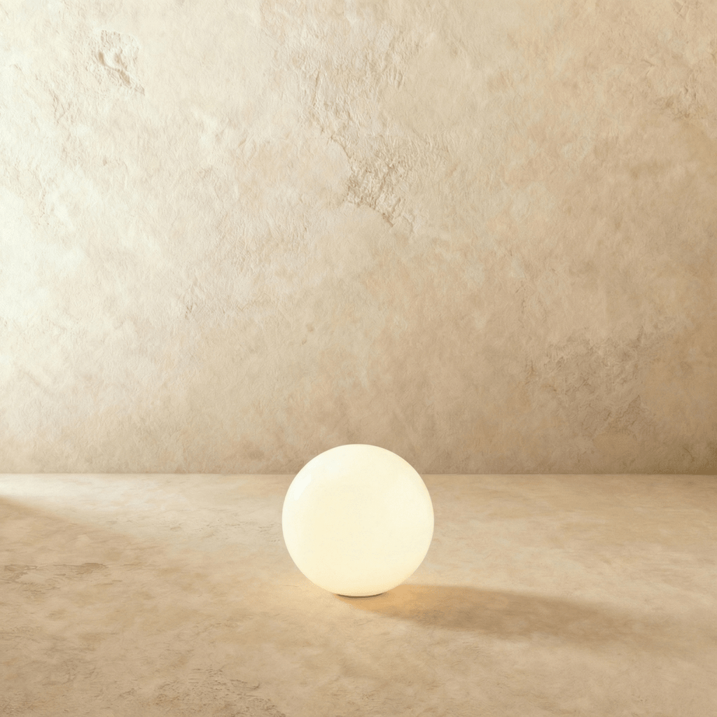 A mid-size Clérachic sphere floor lamp glows brightly against a warm plaster wall and matching floor.