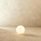 A mid-size Clérachic sphere floor lamp glows brightly against a warm plaster wall and matching floor.