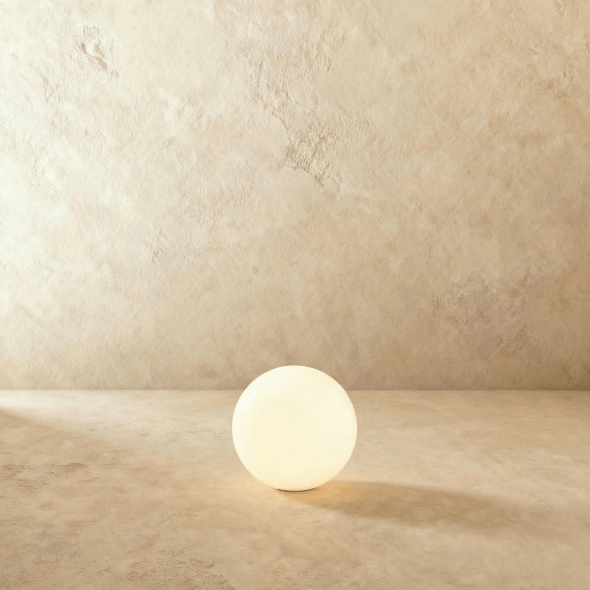 A mid-size Clérachic sphere floor lamp glows brightly against a warm plaster wall and matching floor.
