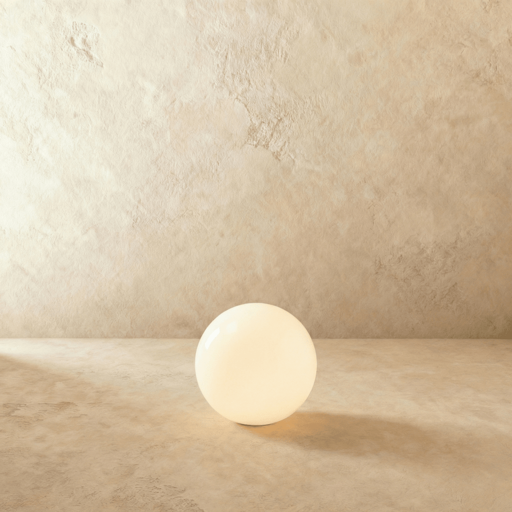 This Clérachic glowing sphere floor lamp sits lit with a soft warm glow on a sandy plaster backdrop.
