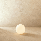 This Clérachic glowing sphere floor lamp sits lit with a soft warm glow on a sandy plaster backdrop.