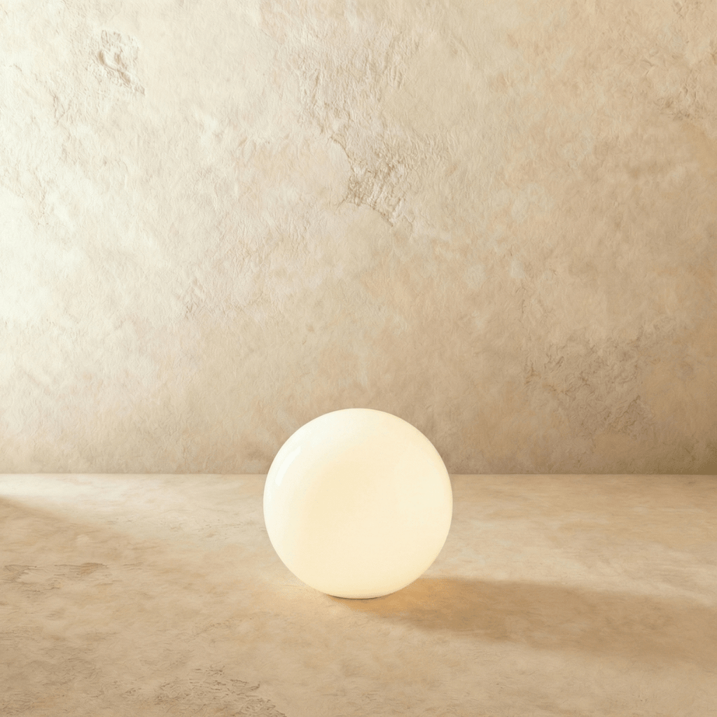 A larger unlit Clérachic sphere floor lamp shows its glossy opal surface against a plaster wall.