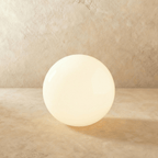 A large Clérachic sphere floor lamp glows warm at its base, set against a sandy plaster backdrop.
