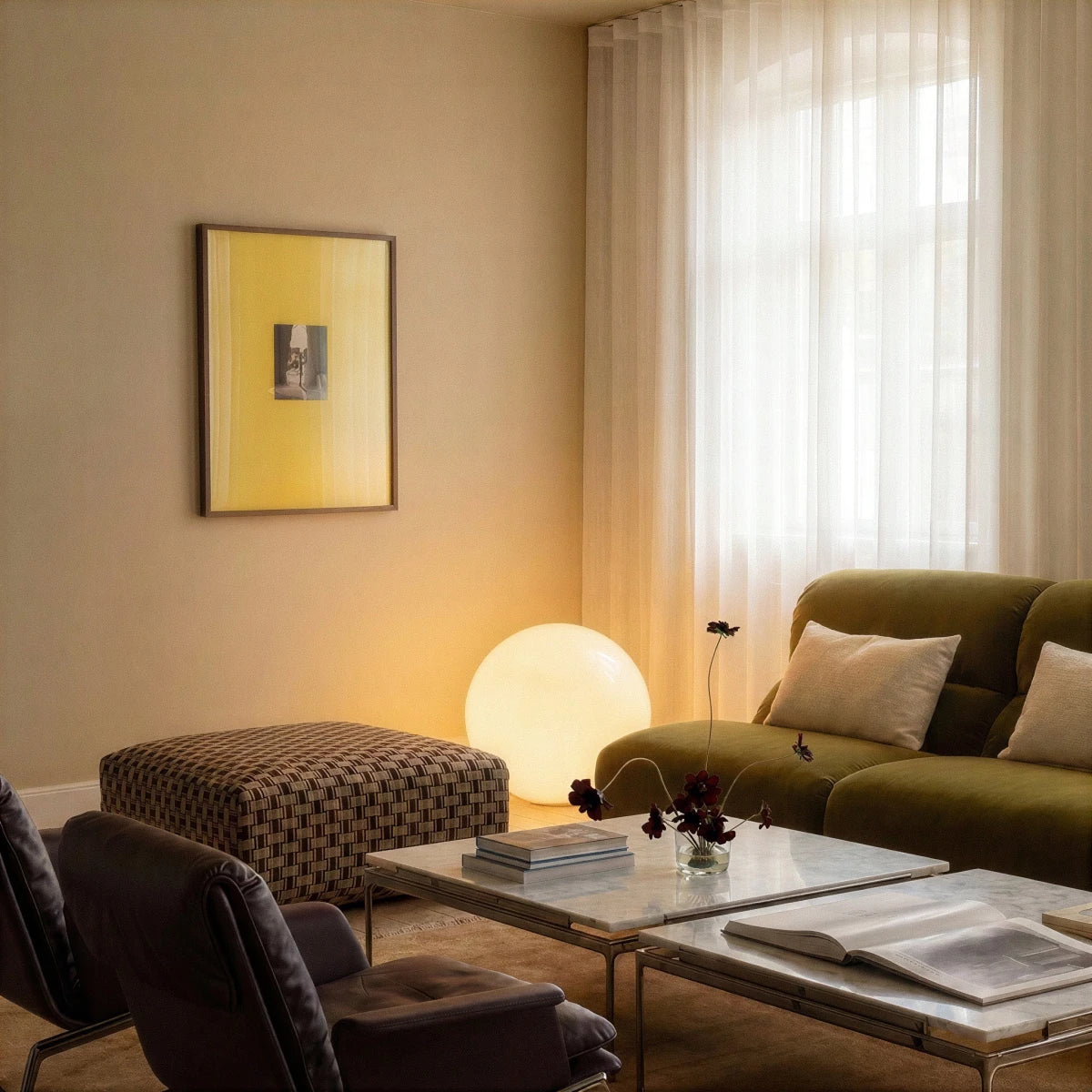 A lit Clérachic sphere floor lamp glows beside a green sofa in a living room with sheer curtains and art.