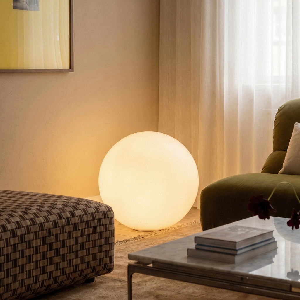 Close view of the lit Clérachic sphere floor lamp glowing beside a checked ottoman and marble coffee table.