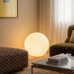 Close view of the lit Clérachic sphere floor lamp glowing beside a checked ottoman and marble coffee table.