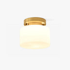 This Clérachic flush-mount ceiling light on a plain white backdrop, a round brass canopy above a white cylindrical glass shade.