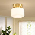 A Clérachic flush-mount light with a white glass drum shade and brass canopy, hung in a bright room beside a sheer curtain and a fig plant.