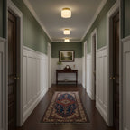 Three Clérachic flush-mount lights run down a sage-green hallway with white panelling, dark doors and a blue-patterned runner.