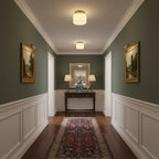 Two Clérachic brass and white glass ceiling lights over a green-walled entry, with a console table, table lamps and gilt-framed landscapes.