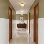 A Clérachic flush-mount light in a hallway of sage-green walls, white panelling and warm wooden doors, with a sideboard at the far end.