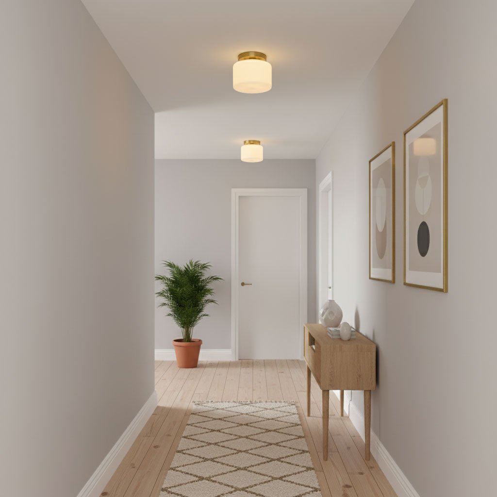 A Clérachic flush-mount ceiling light in a pale grey hallway, with a light oak console, a potted palm and two framed abstract prints.
