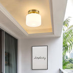 A Clérachic white glass flush-mount light glowing in a recessed cream ceiling, beside a balcony window and a framed 'Simplicity' print.