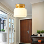Close view of this Clérachic flush-mount light above a doorway, with a dark wood door, glazed panels and a small console with plants below.