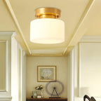 A Clérachic white drum flush-mount light under a pale yellow ceiling with cornice mouldings, above a console with a framed print and flowers.
