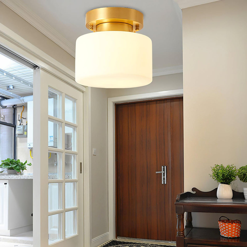 This Clérachic flush-mount light above a wooden door with glazed side panels, a carved console and a small potted plant beneath.