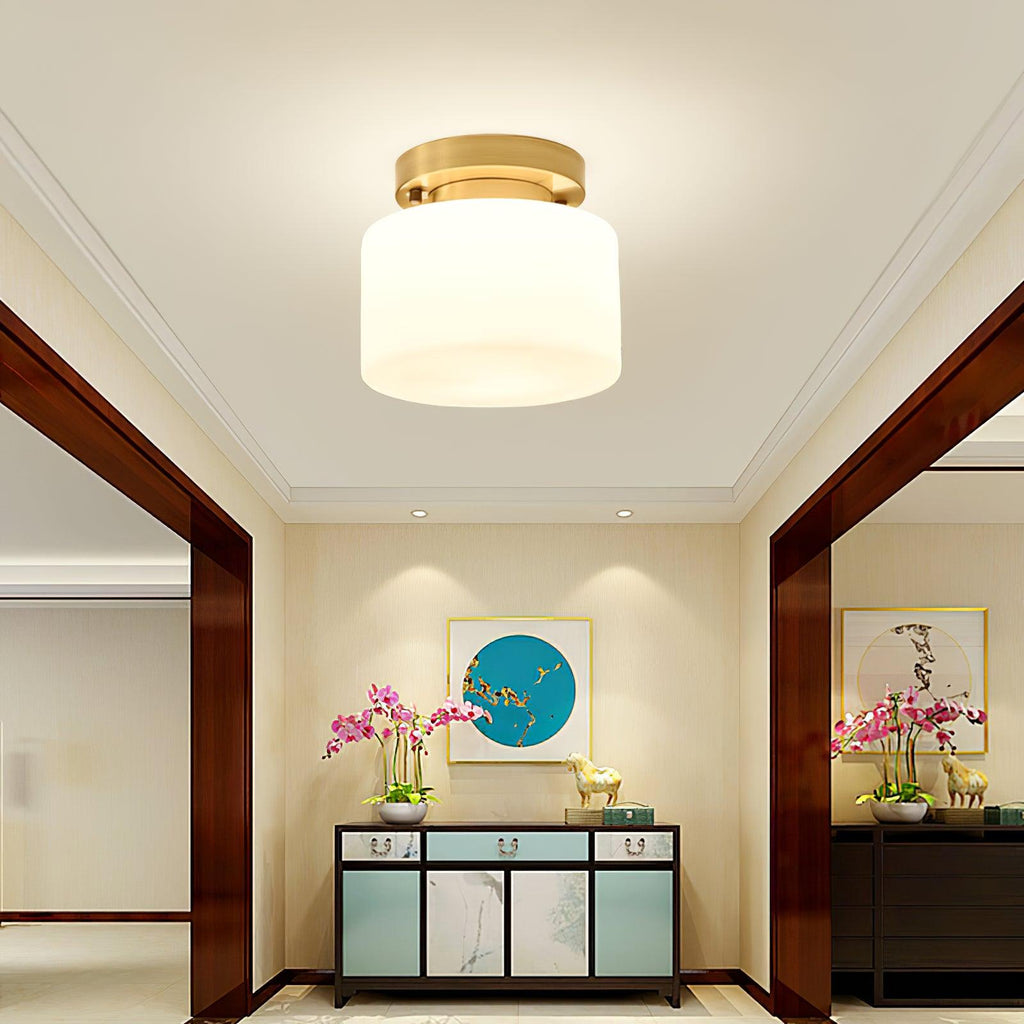 A Clérachic brass and white glass flush-mount light in a symmetrical entry with dark wood trim, a teal console and pink orchids.
