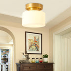 A Clérachic white drum flush-mount light close up, with a cream arched doorway, a framed Venetian print and a dark wooden sideboard below.