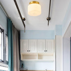 A Clérachic flush-mount light on a pale ceiling next to dark curtain rails, with a blue wall, curtains and white cabinets in the room.
