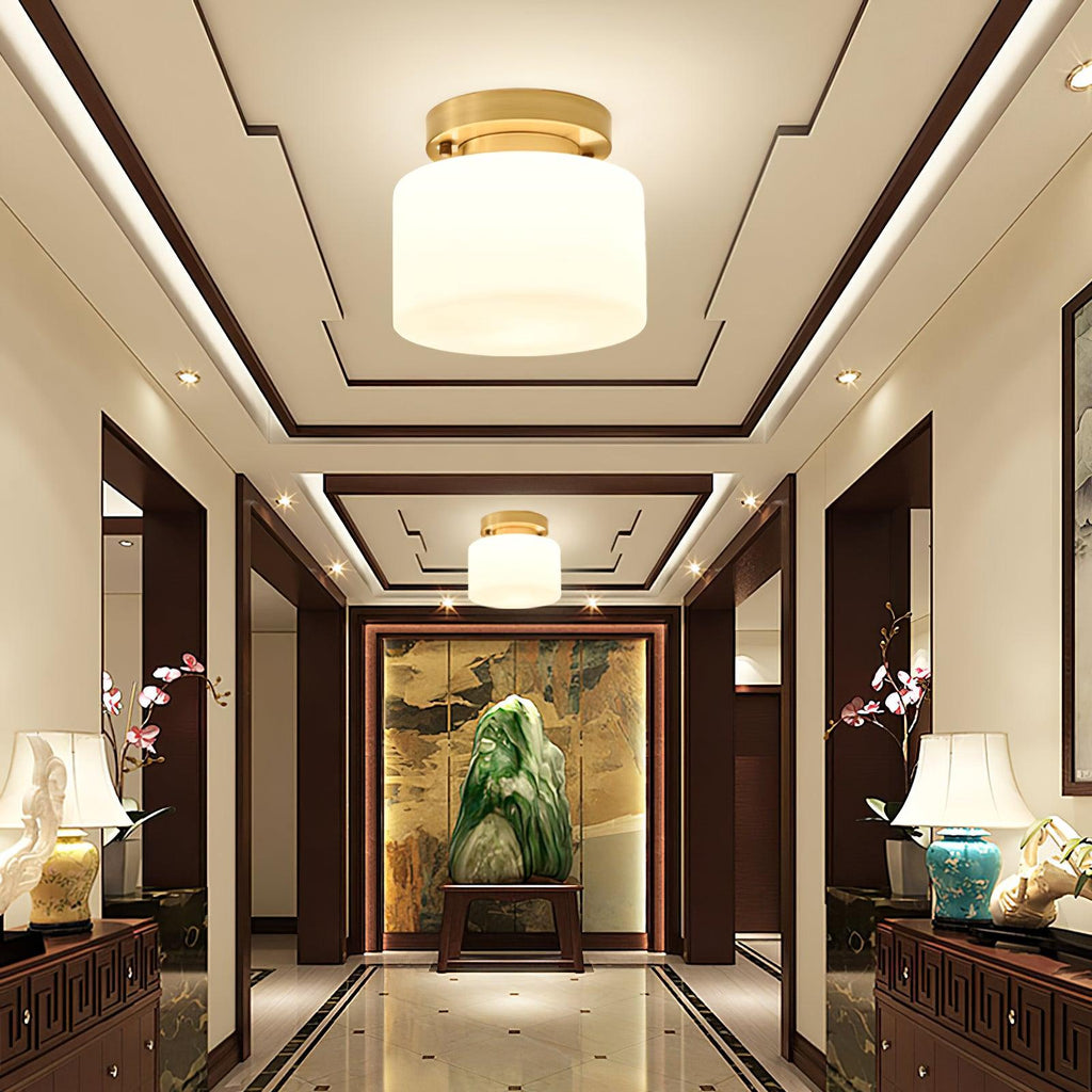 A Clérachic brass and white glass flush-mount light in a grand hallway with a coffered ceiling, polished floor and lamps on dark cabinets.