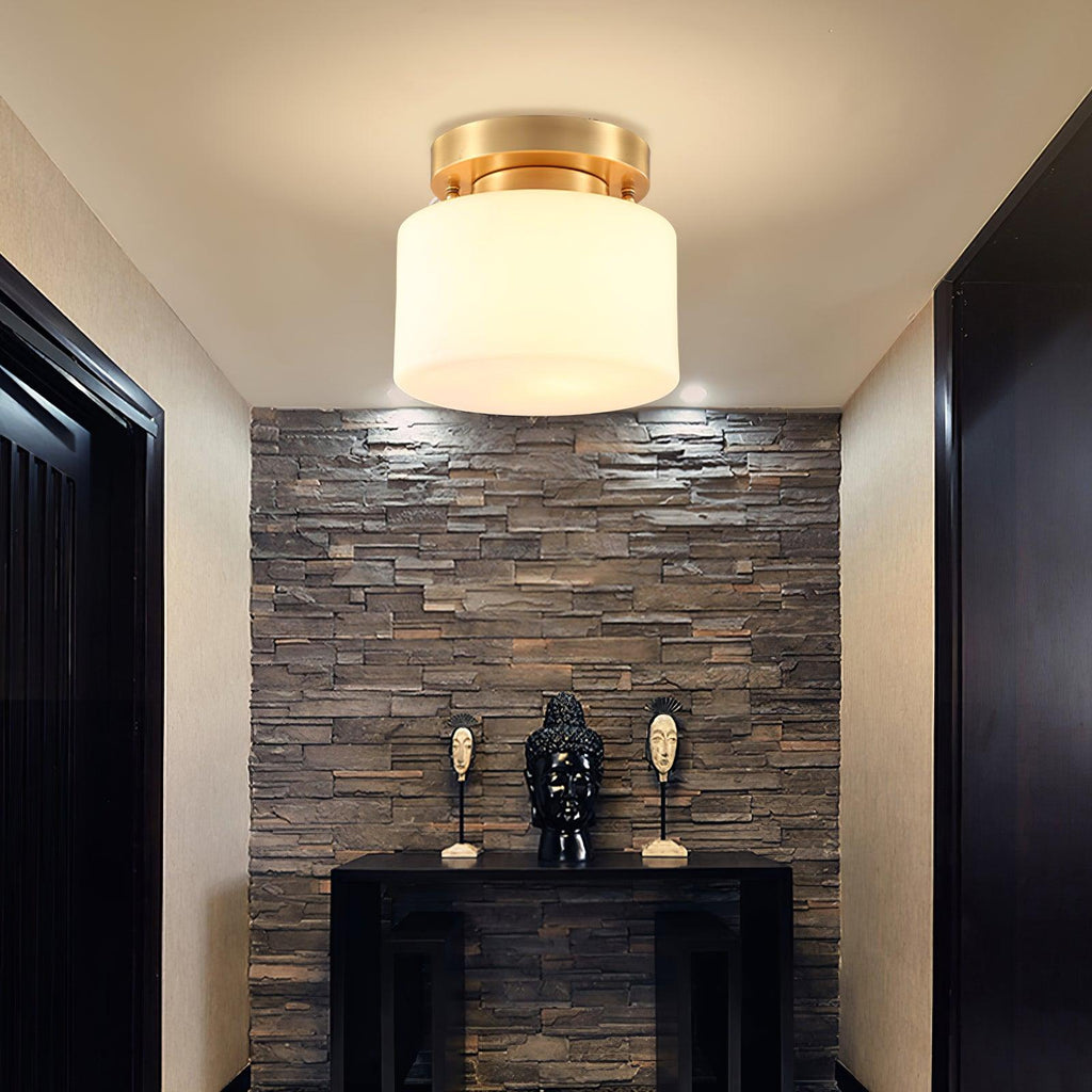 A Clérachic flush-mount light glowing above a dark entry with a stacked-stone feature wall and a black console with two carved figures.