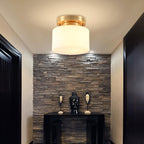 A Clérachic flush-mount light glowing above a dark entry with a stacked-stone feature wall and a black console with two carved figures.
