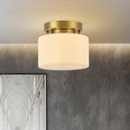 A Clérachic flush-mount ceiling light seen against a grey textured plaster wall, with a white arched architectural print at the lower corner.