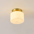 Close view of this Clérachic flush-mount light on a soft beige ceiling, a white glass drum shade under a small brass canopy.