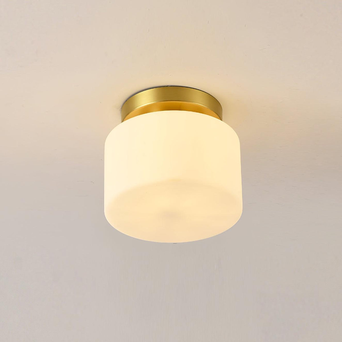 Close view of this Clérachic flush-mount light on a soft beige ceiling, a white glass drum shade under a small brass canopy.