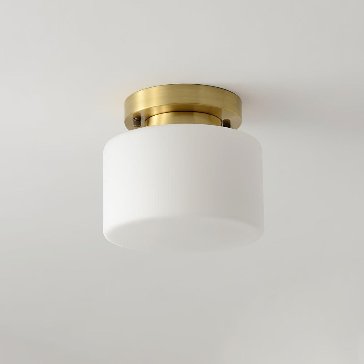 This Clérachic flush-mount light on a pale grey ceiling, showing the white glass drum shade and the slim brass canopy with two small screws.