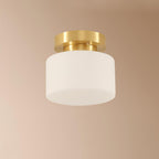 A Clérachic flush-mount light against a blush-beige ceiling, with a frosted white glass shade and a brushed brass canopy.