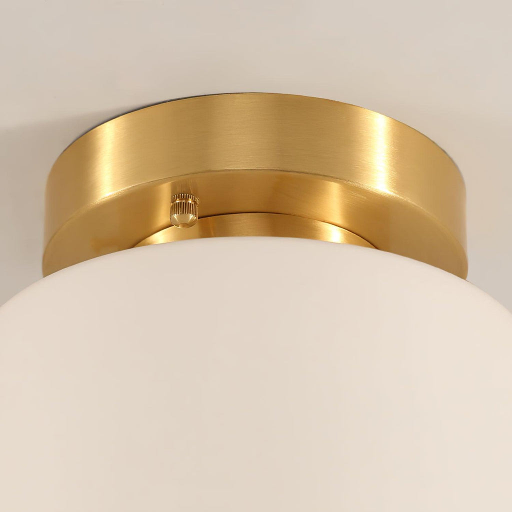 Close view of the brushed brass canopy and small fixing screw on this Clérachic flush-mount light, with the white glass shade below.