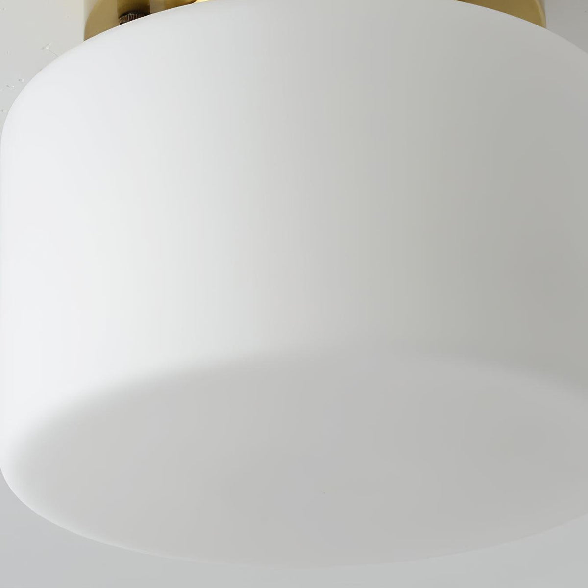 Close view of the smooth, frosted white glass drum shade on this Clérachic flush-mount light, with a hint of the brass canopy at the top.