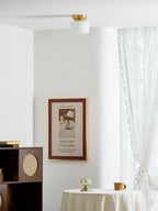 Wider view of a bright room with a Clérachic flush-mount light on the ceiling, a framed print, a rattan cabinet and a table with a lace cloth.