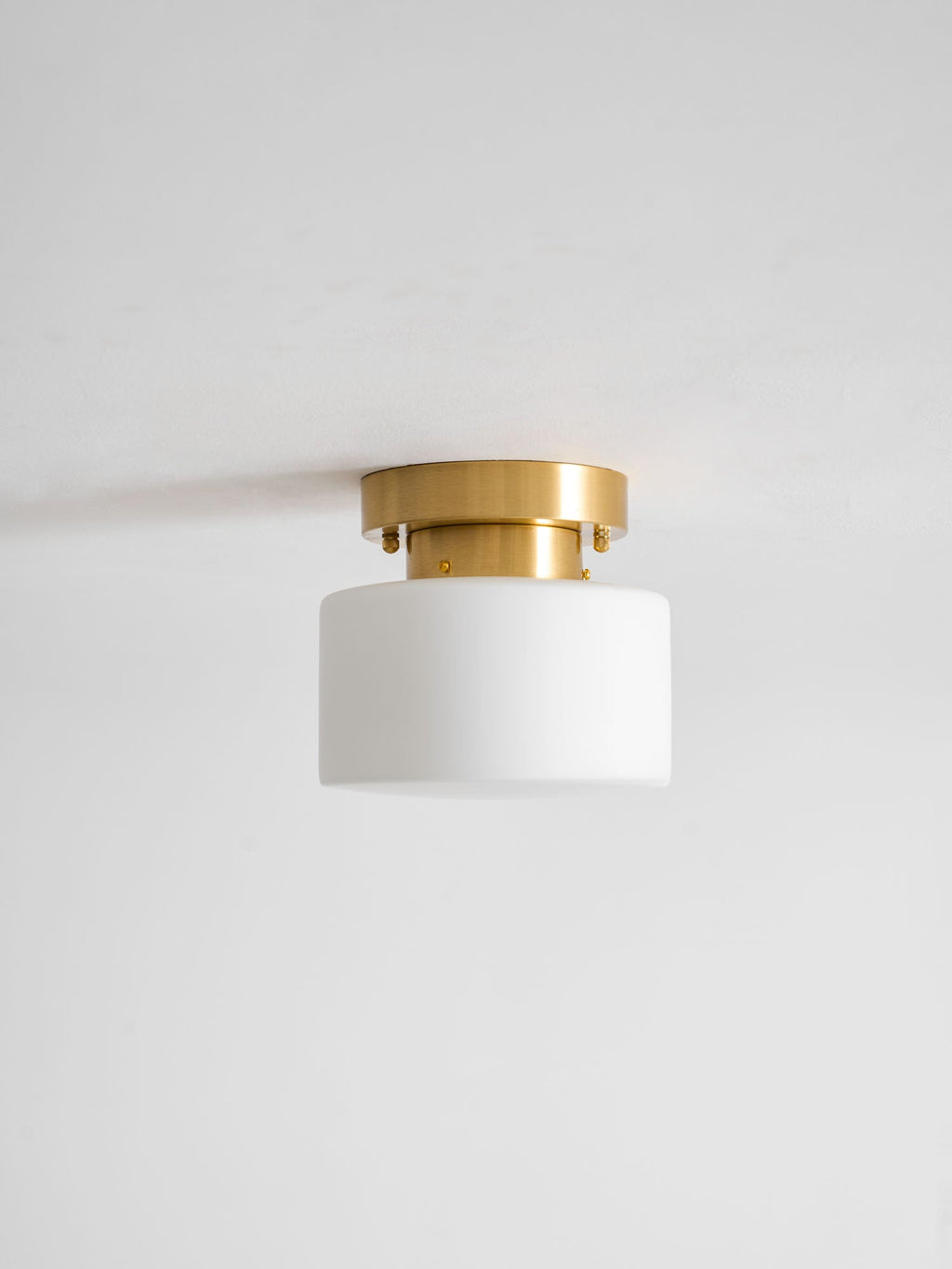 Unlit Clérachic flush-mount light with a white glass drum shade and brushed brass canopy against a pale grey ceiling.