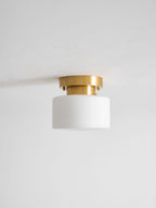 Unlit Clérachic flush-mount light with a white glass drum shade and brushed brass canopy against a pale grey ceiling.